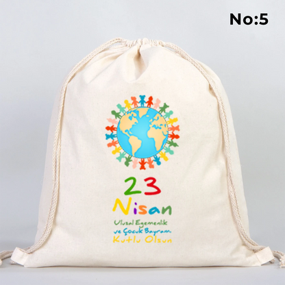 40x50 cm naturel renkli büzgülü bez çanta üzerinde “23 Nisan Kutlu Olsun” yazılı renkli çocuk figürleri baskısı, balon detayları ve kutlama temalı sınıf arka planı