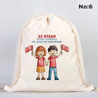 40x50 cm naturel renkli büzgülü bez çanta üzerinde “23 Nisan Kutlu Olsun” yazılı renkli çocuk figürleri baskısı, balon detayları ve kutlama temalı sınıf arka planı