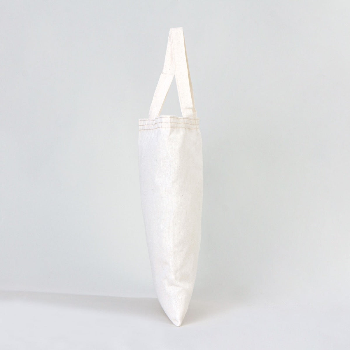 Rengarenk ve sıcak bir sınıf ortamında, ahşap masada sergilenen 30x35 cm kısa kulplu ham pamuk bez çanta.