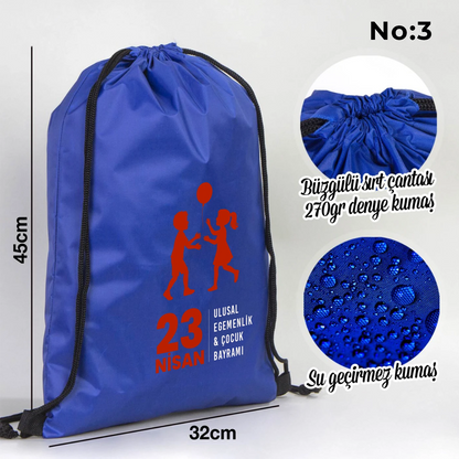 32x45 cm mavi büzgülü sırt çantası üzerinde dünya figürü, renkli çocuk silüetleri ve “23 Nisan Ulusal Egemenlik ve Çocuk Bayramı Kutlu Olsun” yazılı baskı, sınıf temalı arka plan