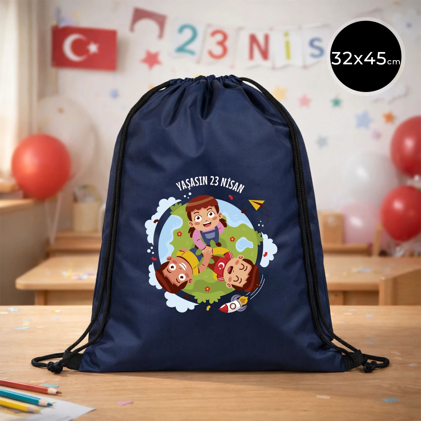 32x45 cm lacivert büzgülü sırt çantası üzerinde “Yaşasın 23 Nisan” yazılı çocuk temalı renkli baskı, roket ve kâğıt uçak detayları, kutlama temalı sınıf arka planı