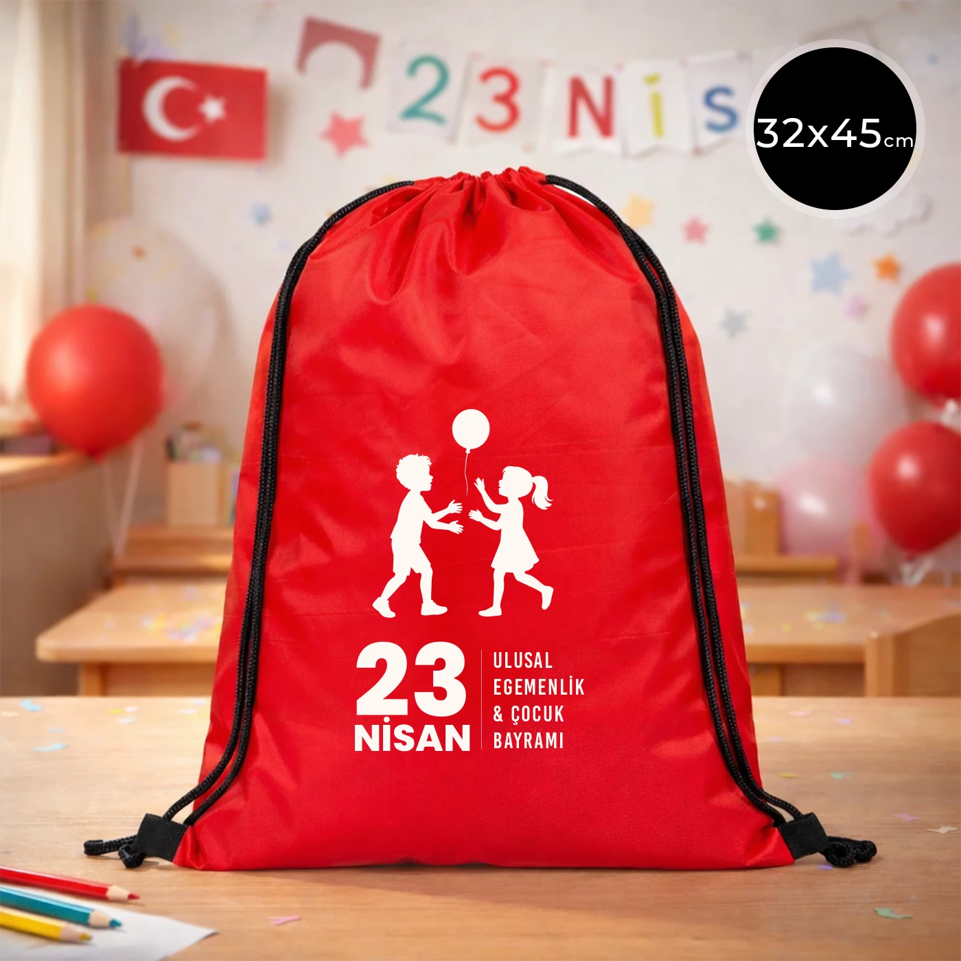32x45 cm kırmızı büzgülü sırt çantası üzerinde beyaz “23 Nisan Ulusal Egemenlik ve Çocuk Bayramı” baskısı, balonlu çocuk figürleri ve kutlama temalı sınıf arka planı