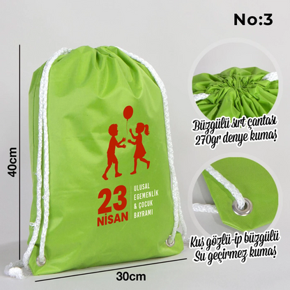 32x45 cm yeşil büzgülü sırt çantası üzerinde dünya figürü, renkli çocuk silüetleri ve “23 Nisan Ulusal Egemenlik ve Çocuk Bayramı Kutlu Olsun” yazılı baskı, kutlama temalı sınıf arka planı