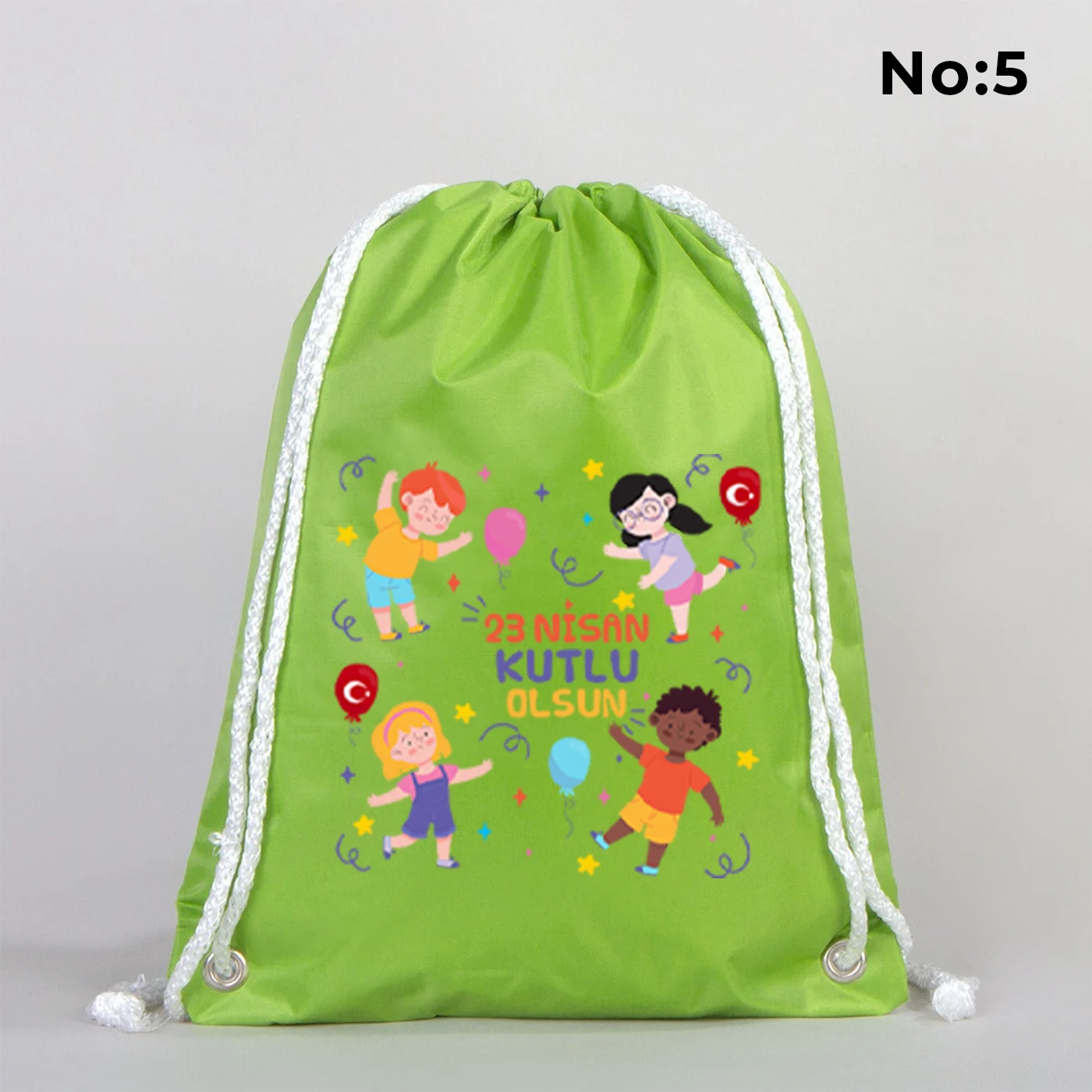 32x45 cm yeşil büzgülü sırt çantası üzerinde dünya figürü, renkli çocuk silüetleri ve “23 Nisan Ulusal Egemenlik ve Çocuk Bayramı Kutlu Olsun” yazılı baskı, kutlama temalı sınıf arka planı