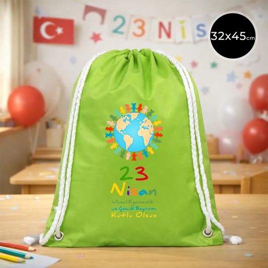32x45 cm yeşil büzgülü sırt çantası üzerinde dünya figürü, renkli çocuk silüetleri ve “23 Nisan Ulusal Egemenlik ve Çocuk Bayramı Kutlu Olsun” yazılı baskı, kutlama temalı sınıf arka planı