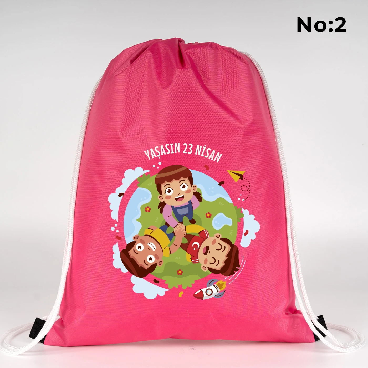 32x45 cm pembe büzgülü sırt çantası üzerinde “23 Nisan Kutlu Olsun” yazılı renkli çocuk figürleri baskısı, balon detayları ve kutlama temalı sınıf arka planı