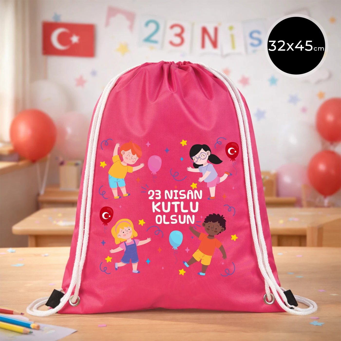 32x45 cm pembe büzgülü sırt çantası üzerinde “23 Nisan Kutlu Olsun” yazılı renkli çocuk figürleri baskısı, balon detayları ve kutlama temalı sınıf arka planı