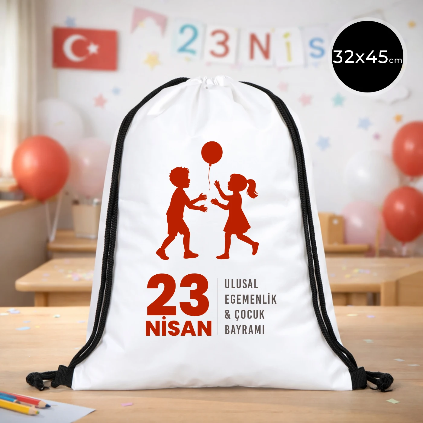 32x45 cm beyaz büzgülü sırt çantası üzerinde kırmızı “23 Nisan Ulusal Egemenlik ve Çocuk Bayramı” baskısı, balonlu çocuk figürleri ve kutlama temalı sınıf arka planı