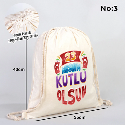 35x40 cm naturel renkli büzgülü bez çanta üzerinde “Yaşasın 23 Nisan” yazılı çocuk temalı renkli baskı, roket ve kâğıt uçak detayları, 23 Nisan süslemeli sınıf arka planı