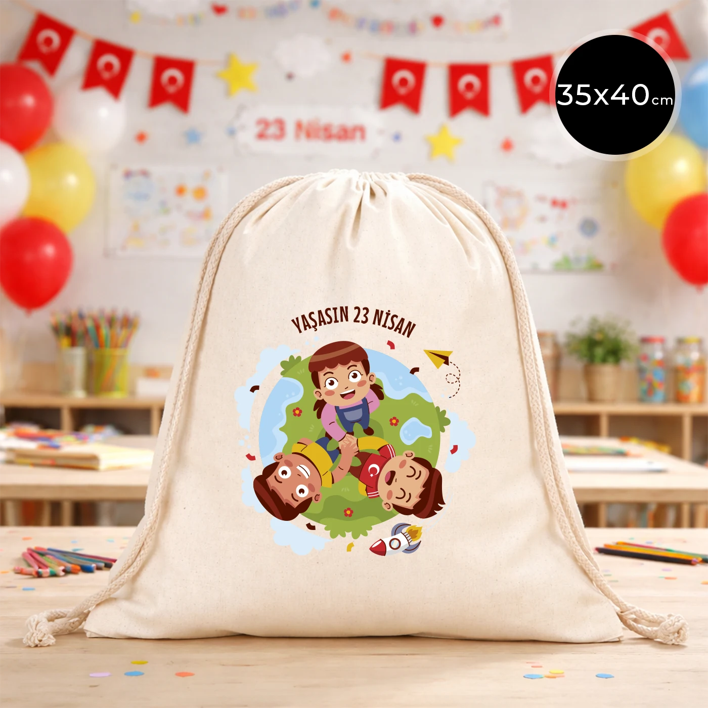 35x40 cm naturel renkli büzgülü bez çanta üzerinde “Yaşasın 23 Nisan” yazılı çocuk temalı renkli baskı, roket ve kâğıt uçak detayları, 23 Nisan süslemeli sınıf arka planı