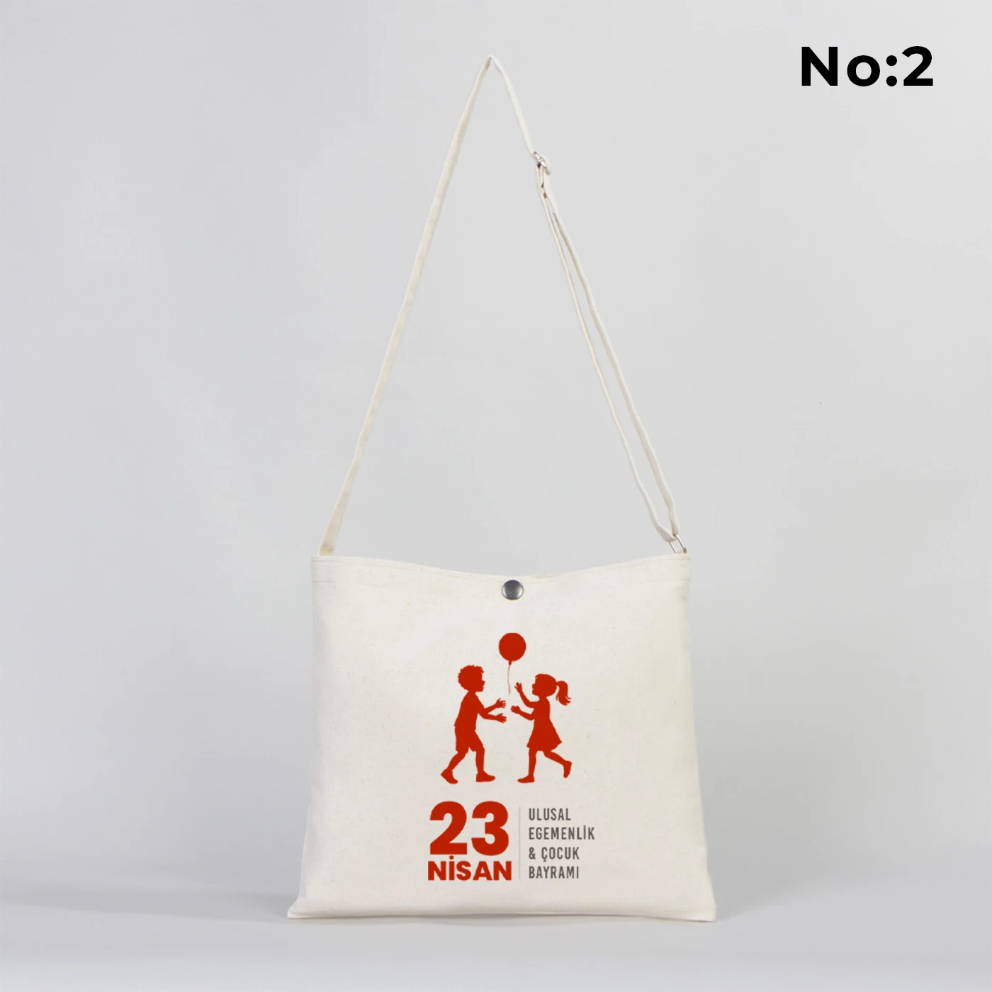 35x30 cm krem renkli çapraz askılı kumaş çanta üzerinde çıtçıt kapama detayı, “23 Nisan Kutlu Olsun” yazılı renkli çocuk figürleri baskısı ve sınıf temalı arka plan