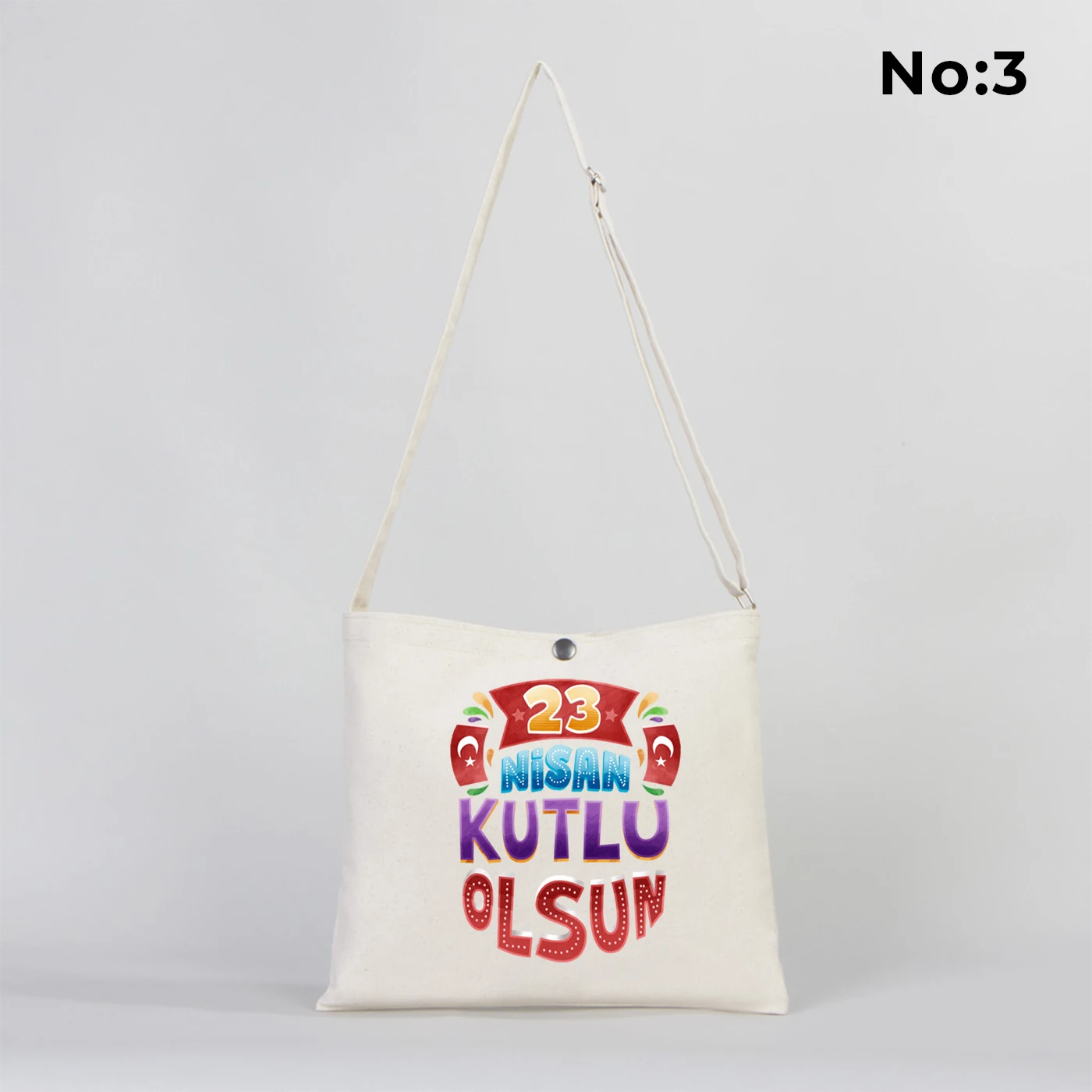 35x30 cm krem renkli çapraz askılı kumaş çanta üzerinde çıtçıt kapama detayı, “23 Nisan Kutlu Olsun” yazılı renkli çocuk figürleri baskısı ve sınıf temalı arka plan