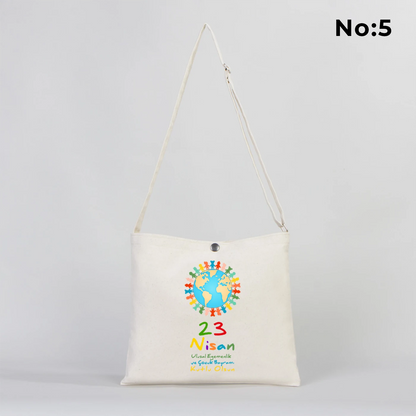 35x30 cm krem renkli çapraz askılı kumaş çanta üzerinde çıtçıt kapama detayı, “23 Nisan Kutlu Olsun” yazılı renkli çocuk figürleri baskısı ve sınıf temalı arka plan