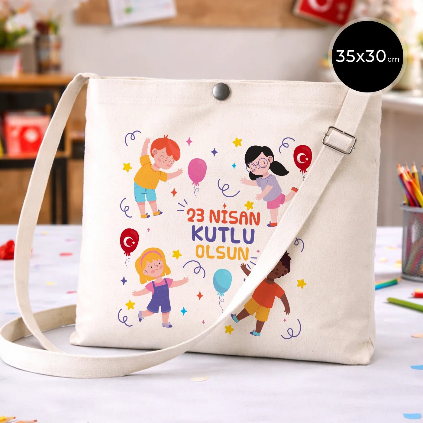 35x30 cm krem renkli çapraz askılı kumaş çanta üzerinde çıtçıt kapama detayı, “23 Nisan Kutlu Olsun” yazılı renkli çocuk figürleri baskısı ve sınıf temalı arka plan