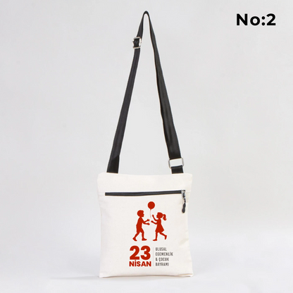 25x28 cm krem renkli çapraz askılı kumaş çanta üzerinde fermuarlı ön cep, “Yaşasın 23 Nisan” yazılı çocuk temalı renkli baskı ve sınıf ortamı arka planı