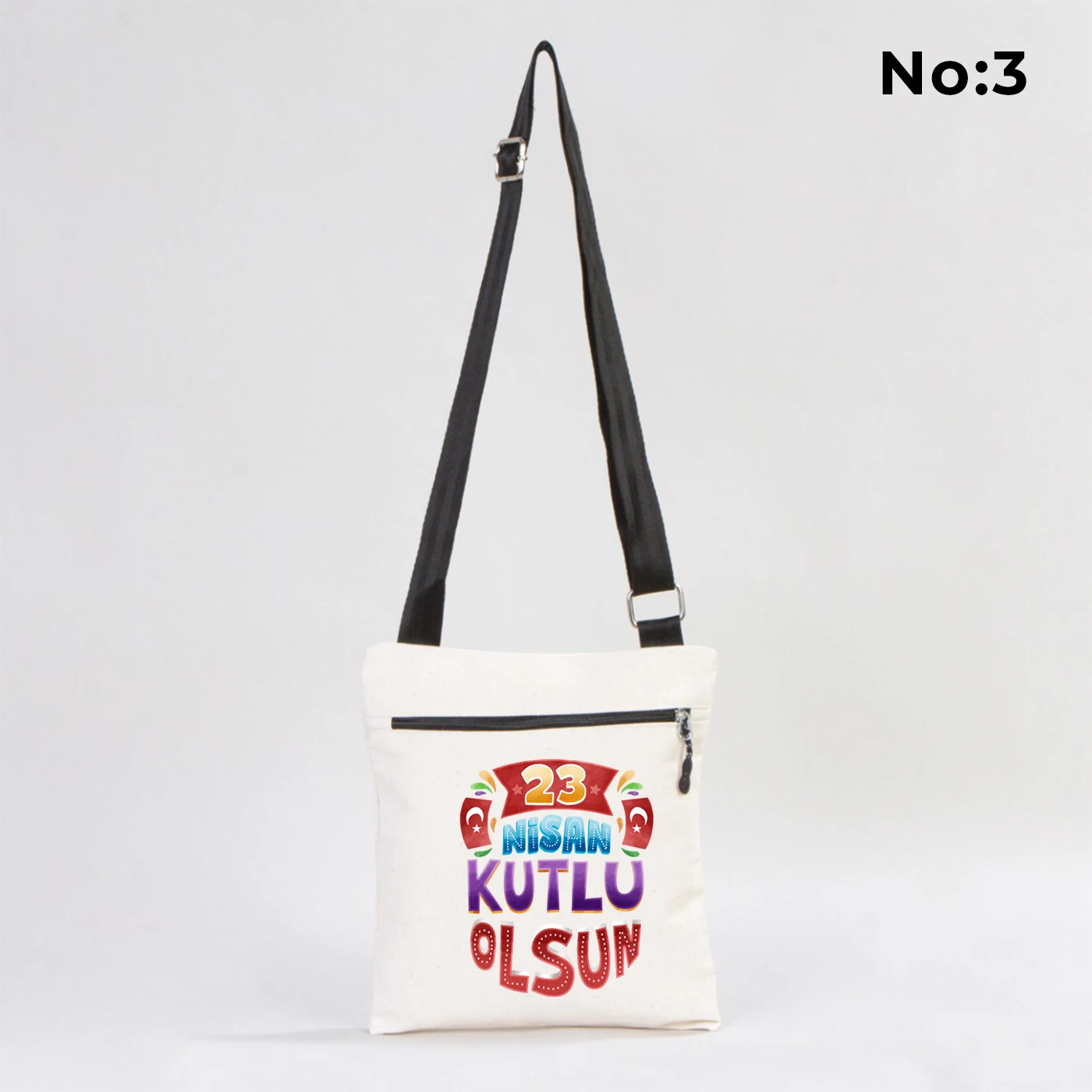 25x28 cm krem renkli çapraz askılı kumaş çanta üzerinde fermuarlı ön cep, “Yaşasın 23 Nisan” yazılı çocuk temalı renkli baskı ve sınıf ortamı arka planı