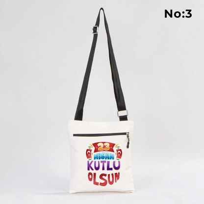 25x28 cm krem renkli çapraz askılı kumaş çanta üzerinde fermuarlı ön cep, “Yaşasın 23 Nisan” yazılı çocuk temalı renkli baskı ve sınıf ortamı arka planı