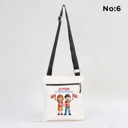 25x28 cm krem renkli çapraz askılı kumaş çanta üzerinde fermuarlı ön cep, “Yaşasın 23 Nisan” yazılı çocuk temalı renkli baskı ve sınıf ortamı arka planı