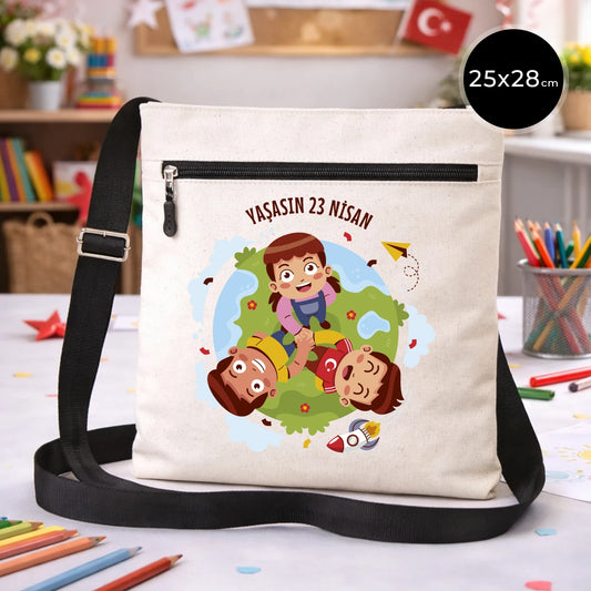 25x28 cm krem renkli çapraz askılı kumaş çanta üzerinde fermuarlı ön cep, “Yaşasın 23 Nisan” yazılı çocuk temalı renkli baskı ve sınıf ortamı arka planı