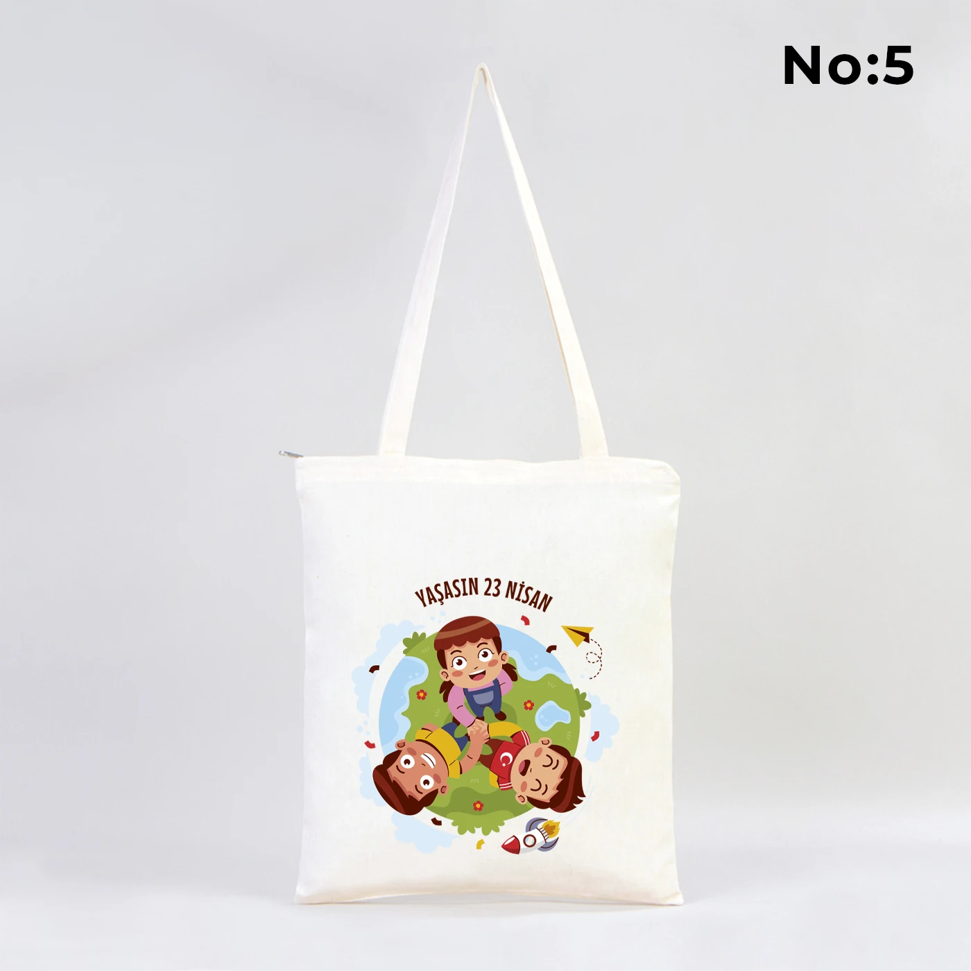 35x40 cm fermuarlı ham bez çanta üzerinde dünya etrafında renkli çocuk figürleri ve “23 Nisan Ulusal Egemenlik ve Çocuk Bayramı Kutlu Olsun” yazısı bulunan 23 Nisan temalı bez çanta.