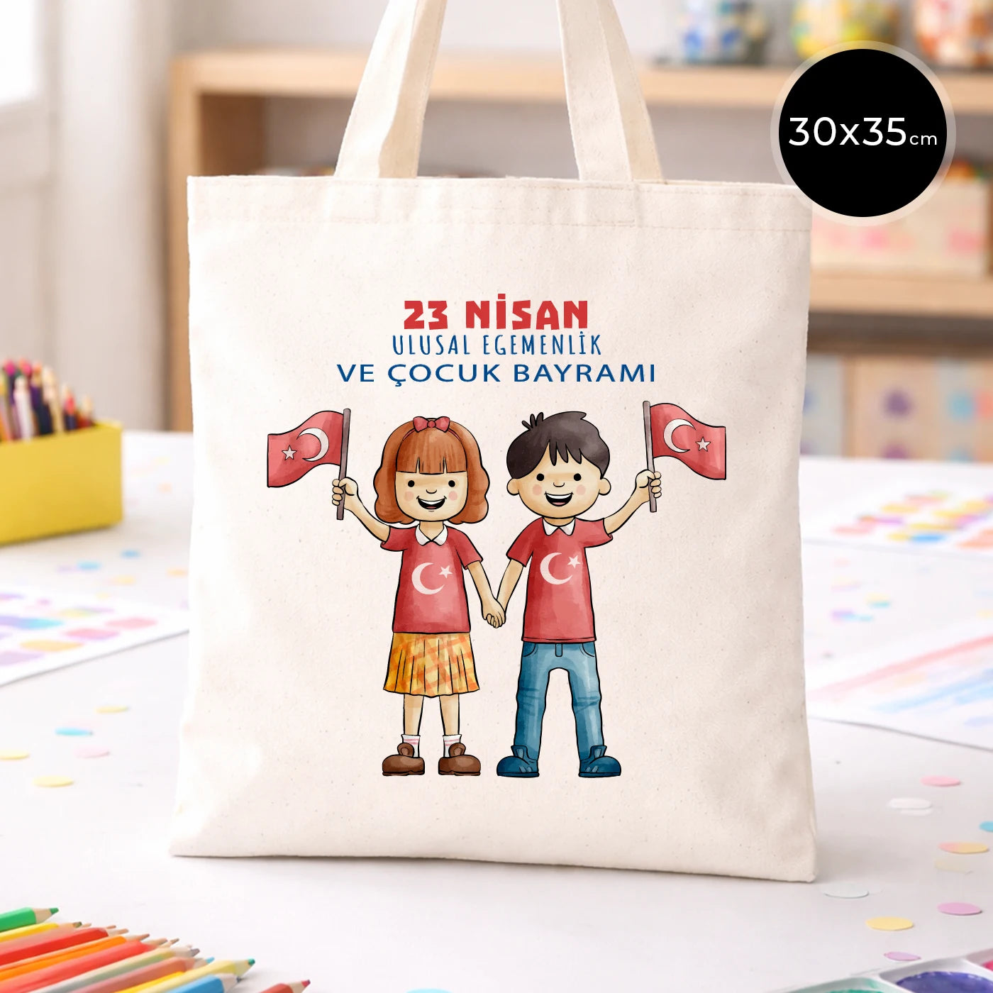 30x35 cm ham bez çanta üzerinde “23 Nisan Ulusal Egemenlik ve Çocuk Bayramı” yazısı ve Türk bayraklı kız-erkek çocuk illüstrasyonu bulunan 23 Nisan temalı bez çanta.