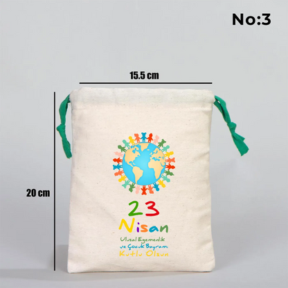 Naturel renkli, yeşil büzgü ipli bez kese üzerinde “Yaşasın 23 Nisan” yazılı çocuk temalı renkli baskı, roket ve kâğıt uçak detayları