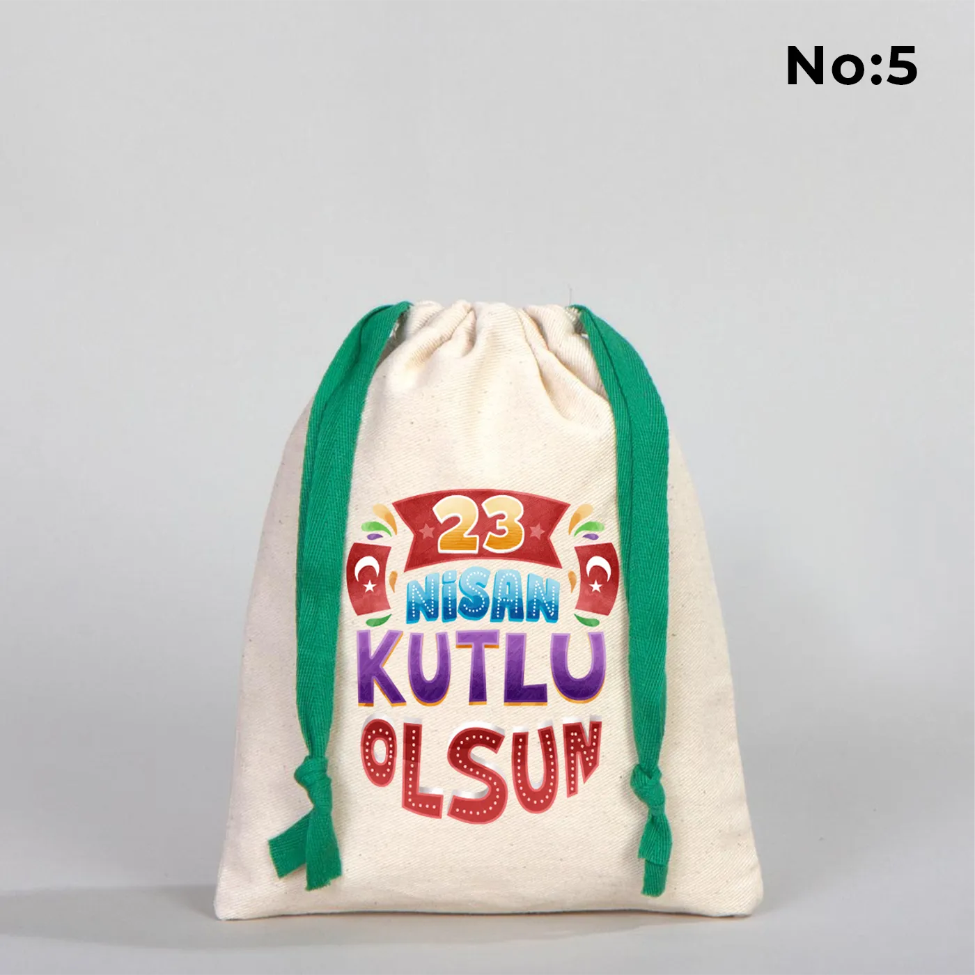 Naturel renkli, yeşil büzgü ipli bez kese üzerinde “Yaşasın 23 Nisan” yazılı çocuk temalı renkli baskı, roket ve kâğıt uçak detayları