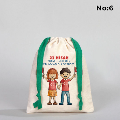 Naturel renkli, yeşil büzgü ipli bez kese üzerinde “Yaşasın 23 Nisan” yazılı çocuk temalı renkli baskı, roket ve kâğıt uçak detayları