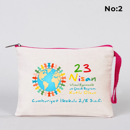 23 Nisan temalı 21x15 cm fermuarlı bez kalemlik üzerinde “23 Nisan Ulusal Egemenlik ve Çocuk Bayramı Kutlu Olsun” yazısı, ay ve yıldız üzerinde oturan iki çocuk illüstrasyonu ve okul - sınıf özelleştirilebilir alan.