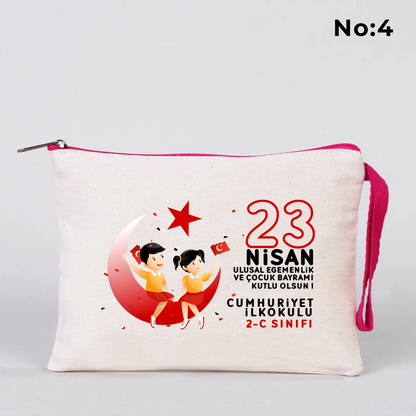 23 Nisan temalı 21x15 cm fermuarlı bez kalemlik üzerinde “23 Nisan Ulusal Egemenlik ve Çocuk Bayramı Kutlu Olsun” yazısı, ay ve yıldız üzerinde oturan iki çocuk illüstrasyonu ve okul - sınıf özelleştirilebilir alan.