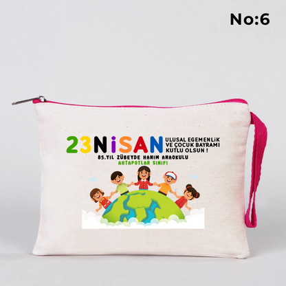 23 Nisan temalı 21x15 cm fermuarlı bez kalemlik üzerinde “23 Nisan Ulusal Egemenlik ve Çocuk Bayramı Kutlu Olsun” yazısı, ay ve yıldız üzerinde oturan iki çocuk illüstrasyonu ve okul - sınıf özelleştirilebilir alan.
