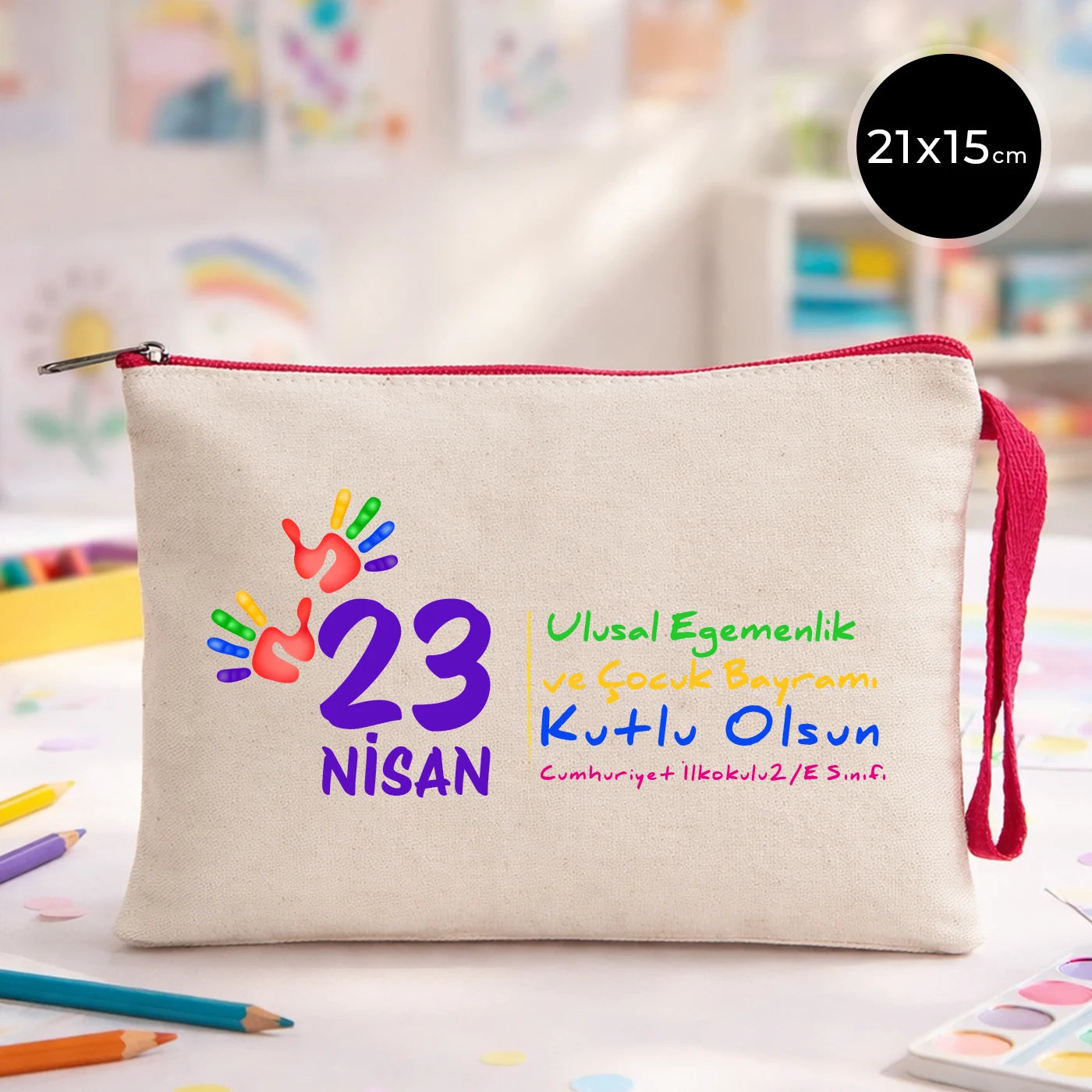 23 Nisan temalı 21x15 cm fermuarlı bez kalemlik üzerinde “23 Nisan Ulusal Egemenlik ve Çocuk Bayramı Kutlu Olsun” yazısı, ay ve yıldız üzerinde oturan iki çocuk illüstrasyonu ve okul - sınıf özelleştirilebilir alan.
