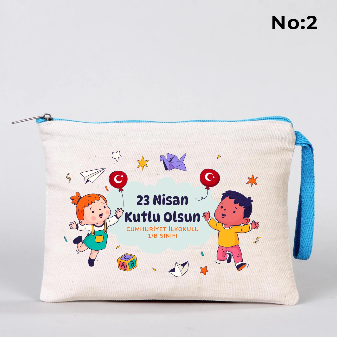 23 Nisan temalı 21x15 cm fermuarlı bez kalemlik üzerinde “23 Nisan Ulusal Egemenlik ve Çocuk Bayramı Kutlu Olsun” yazısı, ay ve yıldız üzerinde oturan iki çocuk illüstrasyonu ve okul - sınıf özelleştirilebilir alan.