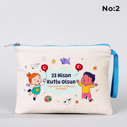 23 Nisan temalı 21x15 cm fermuarlı bez kalemlik üzerinde “23 Nisan Ulusal Egemenlik ve Çocuk Bayramı Kutlu Olsun” yazısı, ay ve yıldız üzerinde oturan iki çocuk illüstrasyonu ve okul - sınıf özelleştirilebilir alan.