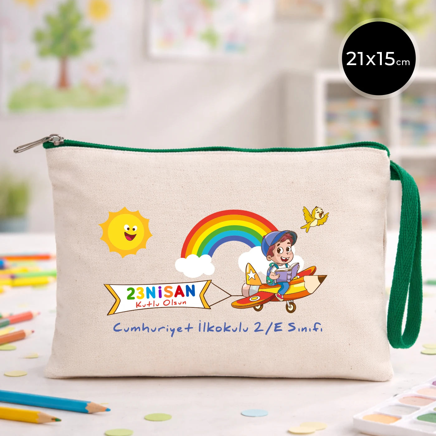 23 Nisan temalı 21x15 cm fermuarlı bez kalemlik üzerinde gökkuşağı, güneş ve uçaklı çocuk illüstrasyonu ile “23 Nisan Kutlu Olsun” yazısı ve okul - sınıf özelleştirilebilir alan.