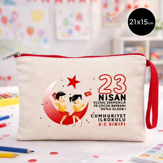 23 Nisan temalı 21x15 cm fermuarlı bez kalemlik üzerinde “23 Nisan Ulusal Egemenlik ve Çocuk Bayramı Kutlu Olsun” yazısı, ay ve yıldız üzerinde oturan iki çocuk illüstrasyonu ve okul - sınıf özelleştirilebilir alan.