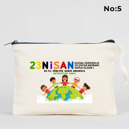 21x15 cm ölçülü, krem renkli fermuarlı kumaş kalemlik üzerinde “23 Nisan Kutlu Olsun” yazısı, balon tutan iki çocuk illüstrasyonu ve sınıf temalı arka plan