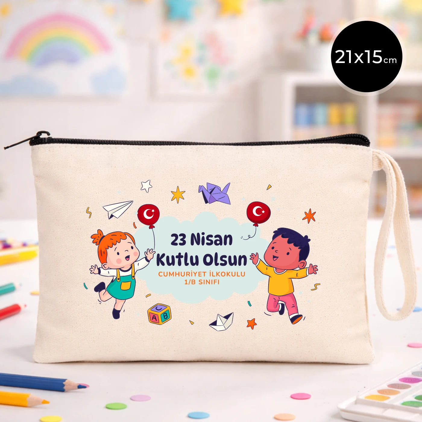 21x15 cm ölçülü, krem renkli fermuarlı kumaş kalemlik üzerinde “23 Nisan Kutlu Olsun” yazısı, balon tutan iki çocuk illüstrasyonu ve sınıf temalı arka plan