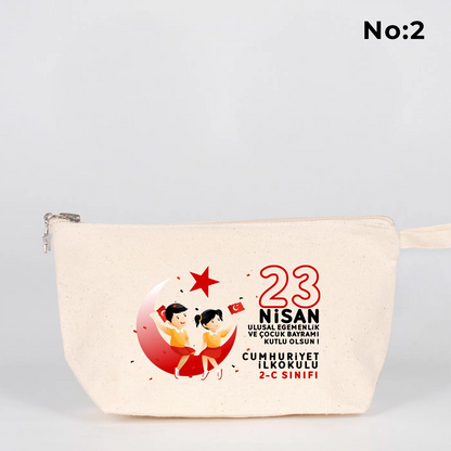 Krem renkli fermuarlı kumaş kalemlik üzerinde ay yıldız üzerinde oturan iki çocuk illüstrasyonu ve “23 Nisan Ulusal Egemenlik ve Çocuk Bayramı Kutlu Olsun” yazılı baskı