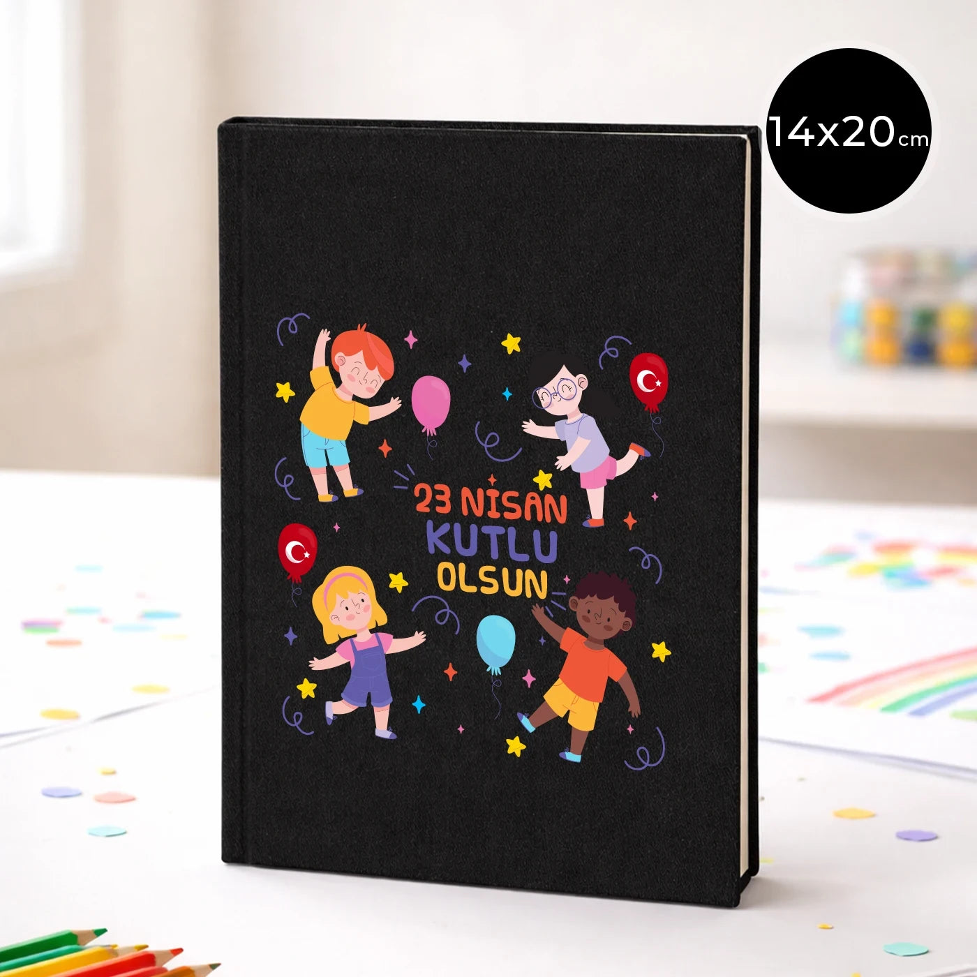 14x20 cm siyah kapaklı defter üzerinde “23 Nisan Kutlu Olsun” yazısı, balonlu ve yıldızlı neşeli çocuk figürleri baskısı, sınıf temalı arka plan