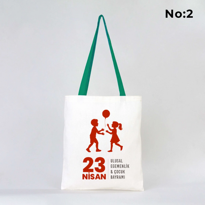 35x40 cm ham bez çanta üzerinde “23 Nisan Ulusal Egemenlik ve Çocuk Bayramı” yazısı ve Türk bayraklı kız-erkek çocuk illüstrasyonu bulunan, yeşil kulplu 23 Nisan temalı bez çanta.