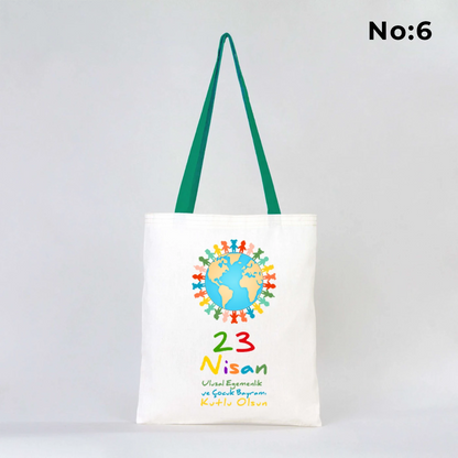 35x40 cm ham bez çanta üzerinde “23 Nisan Ulusal Egemenlik ve Çocuk Bayramı” yazısı ve Türk bayraklı kız-erkek çocuk illüstrasyonu bulunan, yeşil kulplu 23 Nisan temalı bez çanta.