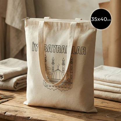 35x40 cm boyanabilir ham bez fermuarlı tote çanta; doğal pamuk kanvas görünüm, ön yüzünde “İyi Bayramlar” yazısı ve cami/minare çizimi bulunan fermuarlı bayram çantası / bayram harçlığı kesesi.