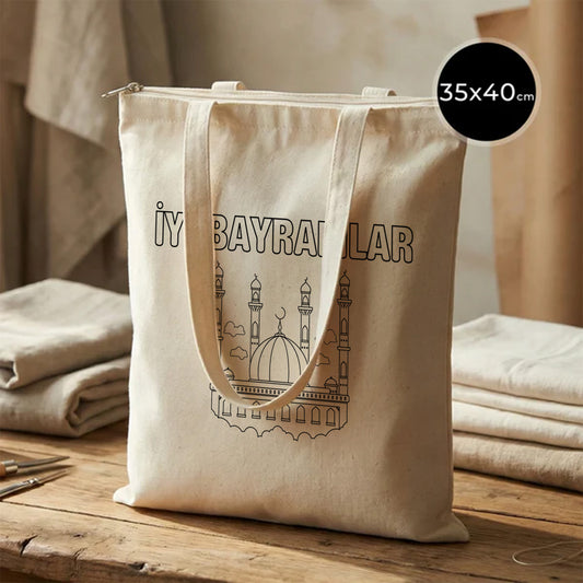 35x40 cm boyanabilir ham bez fermuarlı tote çanta; doğal pamuk kanvas görünüm, ön yüzünde “İyi Bayramlar” yazısı ve cami/minare çizimi bulunan fermuarlı bayram çantası / bayram harçlığı kesesi.