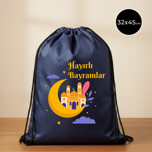 32×45 cm ölçülerinde lacivert ip büzgülü bez sırt çantası üzerinde sarı hilal içinde cami silüeti, mor bulutlar ve yıldızlarla birlikte üstte “Hayırlı Bayramlar” yazısı; siyah ip askılar ve sade açık renkli arka plan.
