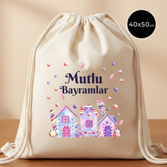 40×50 cm ölçülerinde doğal ham bez büzgülü sırt çantası üzerinde pastel renkli şeker evleri, etrafa saçılmış şeker taneleri ve üstte “Mutlu Bayramlar” yazısı; kalın kordon ipler ve sade açık renkli arka plan.