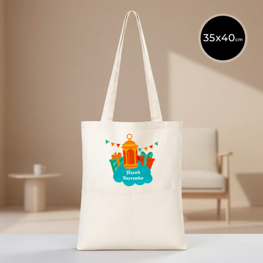 35x40 cm cepli gabardin bez tote çanta, doğal ham renk kumaş, önünde geniş cep bulunan; üzerinde fener, hediye paketleri ve bayraklı “Hayırlı Bayramlar” tasarımı yer alan bayram temalı kanvas alışveriş çantası.