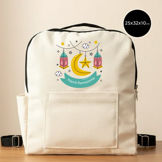 25×32×10 cm ölçülerinde doğal ham bez sırt çantası, siyah fermuar ve askılarla; ön yüzünde asılı pembe–turkuaz fenerler, sarı hilal ve yıldız illüstrasyonu ile turkuaz şerit içinde “Hayırlı Ramazanlar” yazısı ve altında büyük cep bölmesi; sade açık renkli arka plan.