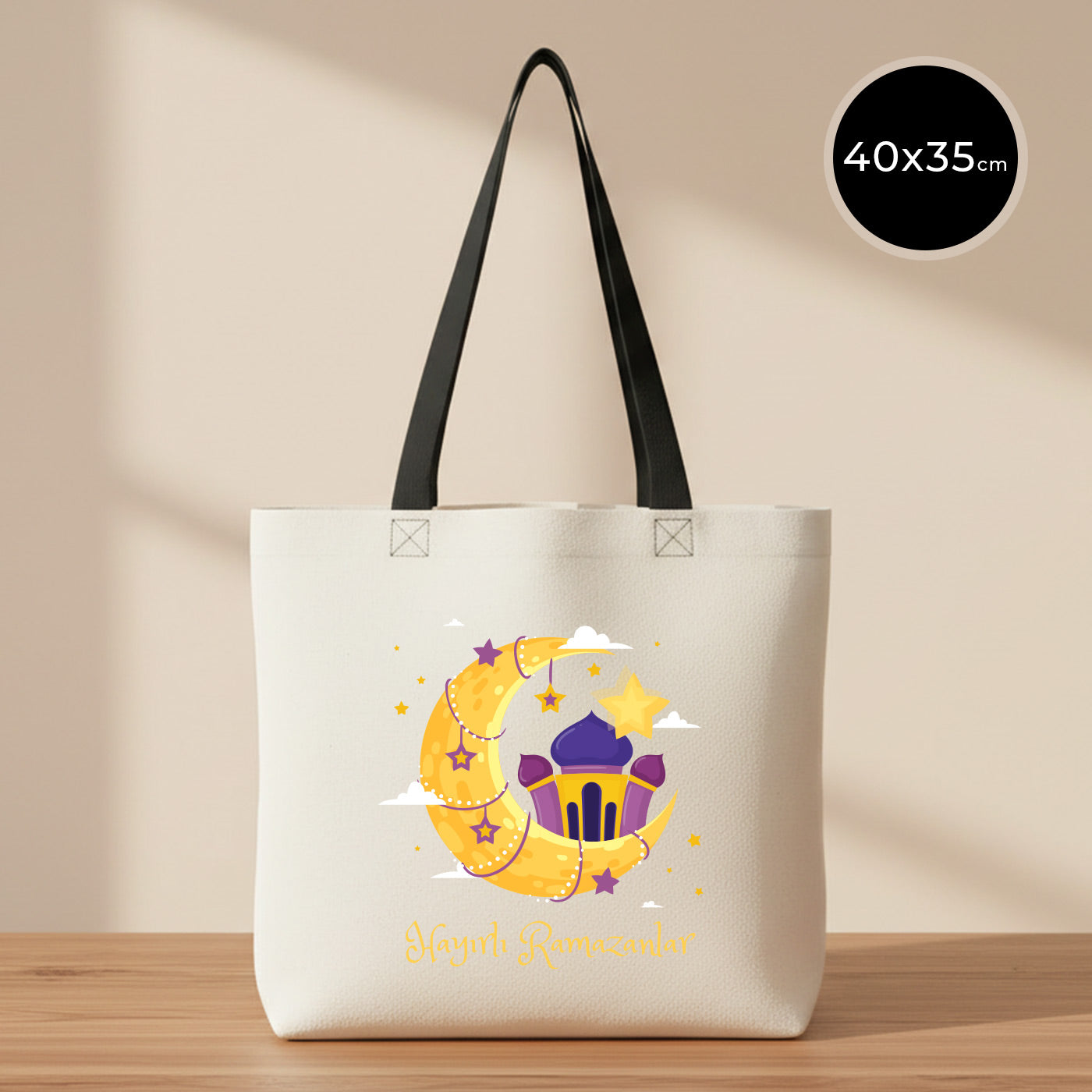 40x35 cm siyah kulplu gabardin bez çanta, krem/ham renk gövde; ön yüzünde ay-yıldız ve cami illüstrasyonlu “Hayırlı Ramazanlar” renkli baskı bulunan Bayram Çantası modeli.