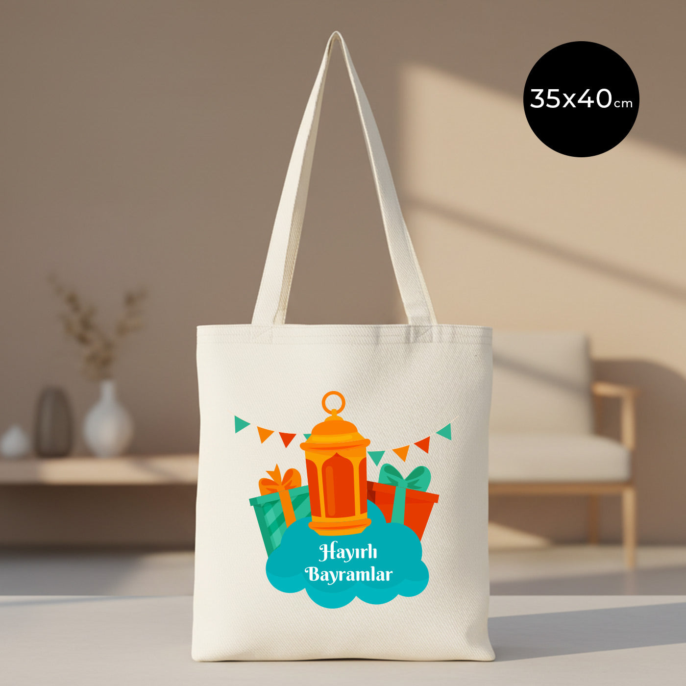 35×40 cm ölçülerinde doğal ham bez tote çanta üzerinde turuncu fener, renkli hediye paketleri ve üçgen bayraklı süslemelerle birlikte mavi bulut zeminde “Hayırlı Bayramlar” yazısı; arka planda sade, aydınlık oturma alanı.